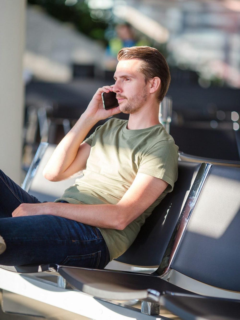 Passenger in a airport lounge waiting for flight aircraft. Young man with cellphone in airport